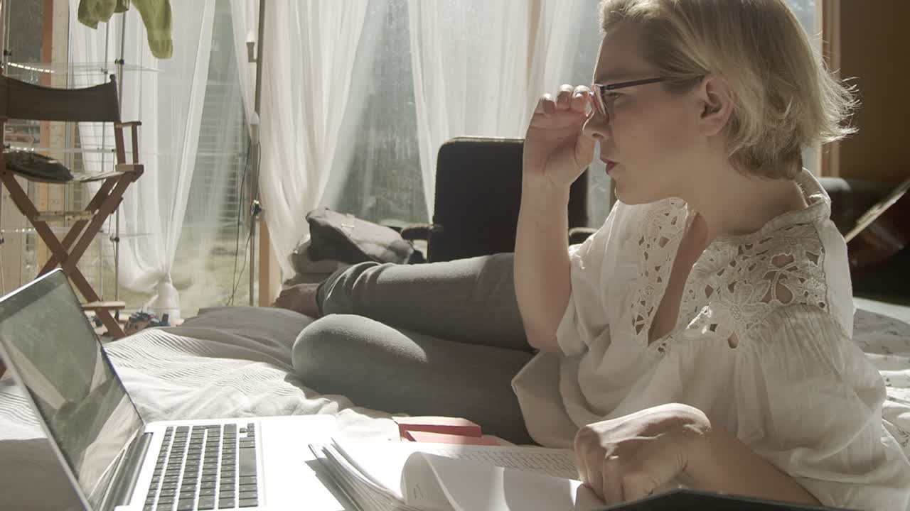 mujer adulta se reclina en la cama mientras trabaja en una laptop en casa