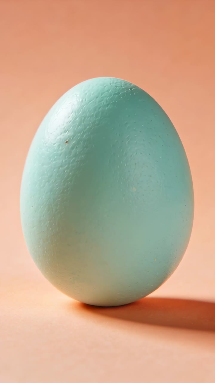 Vertical video: Slight imbalance causing wobbling mint green egg leaning and rolling on peach table