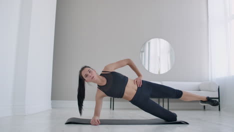 The-brunette-in-the-apartment-does-an-exercise-lateral-plank-standing-on-her-knee-and-raising-her-leg-up.-Fitness-marathon.