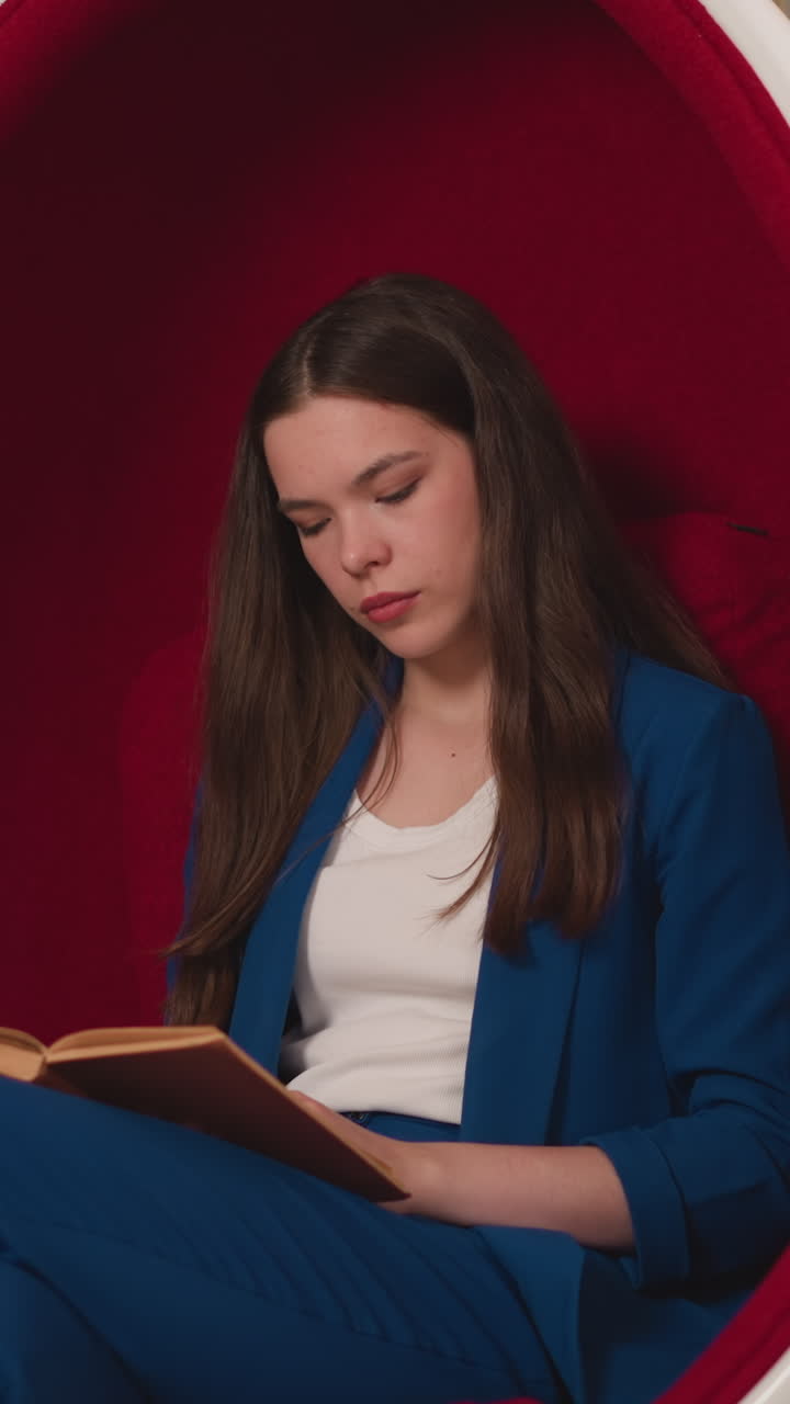 dama en uniforme de oficina lee un libro en una silla de huevo. mujer enfocada se relaja con un libro educativo en un acogedor sillón en un espacio de lectura moderno en la universidad