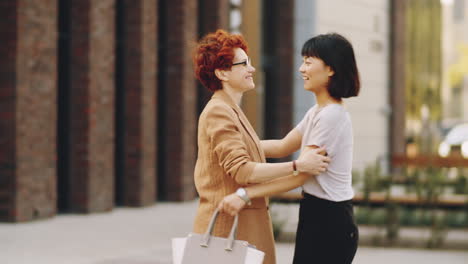 two cheerful women hugging and chatting on street