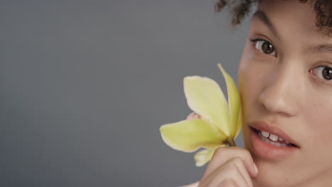 close up portrait beautiful young woman touching skin with orchid flower caressing smooth healthy complexion enjoying natural beauty fragrance on grey background skincare concept