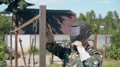 side-view-man-fixes-top-of-metal-fence-with-welding-tool