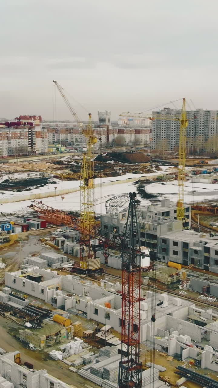 large construction site of white buildings with yellow and orange cranes against residential area on early spring day