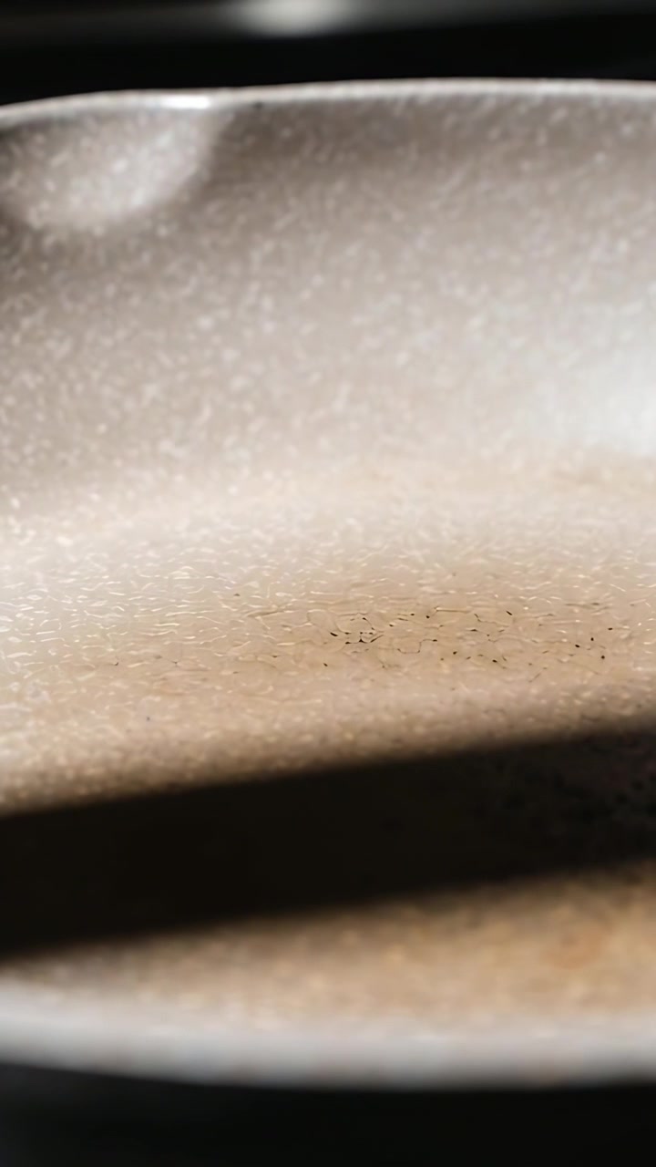 Vertical video: Camera shifting, speckled nonstick pan on stovetop showing dark shadow and residue