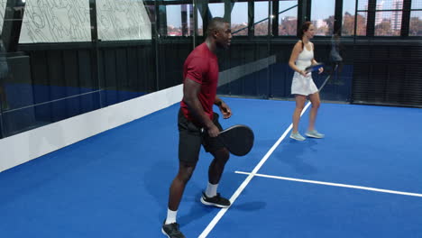 Man and woman playing padel tennis indoors, focusing on intense rally, at indoor court