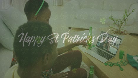 happy st patricks day text and clover leaves against couple having video call on laptop at home