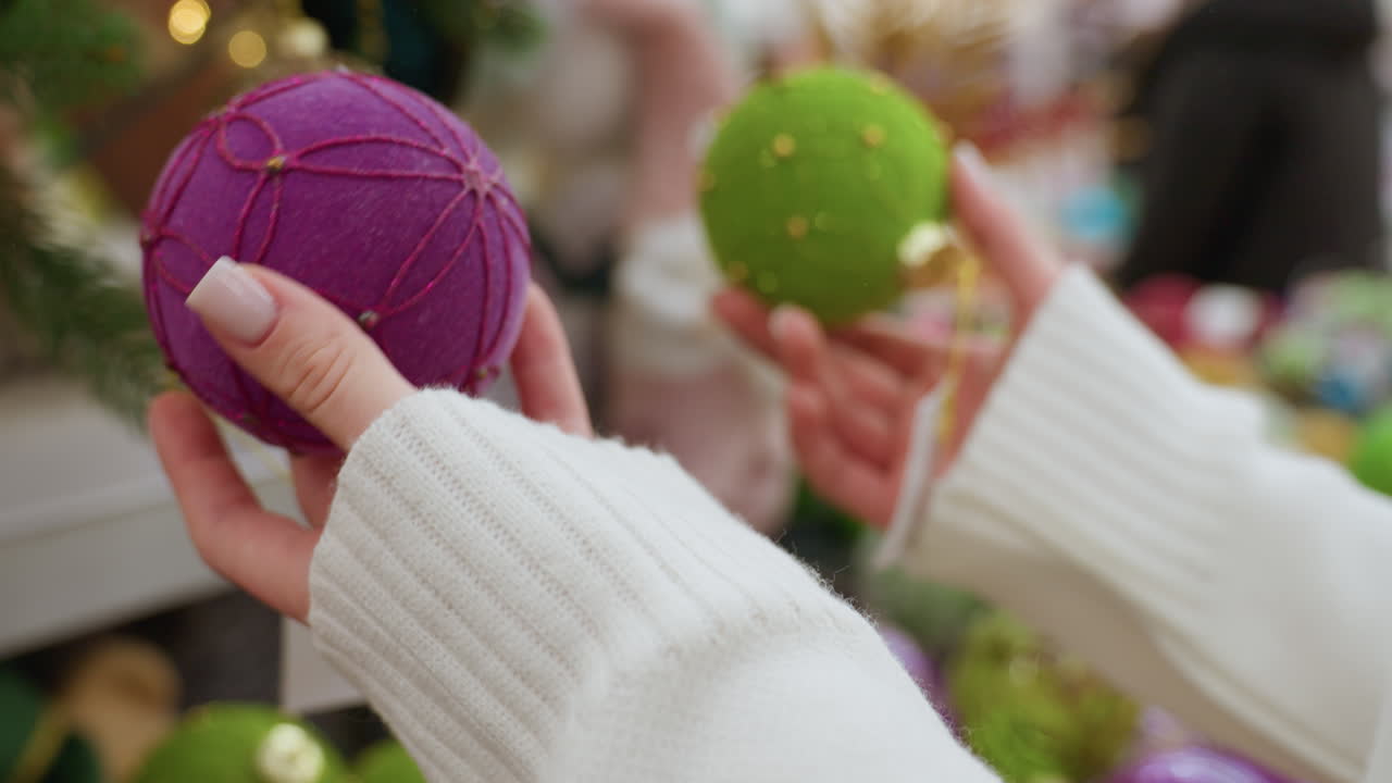 Close up hand view of young lady playfully jamming green and purple decorative balls together while shopping for Christmas ornaments in a festive store