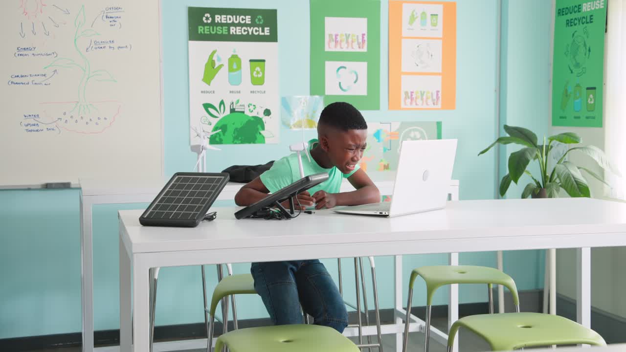African American boy tapping tablet, checking laptop, adjusting solar panel and turbine in STEM lab