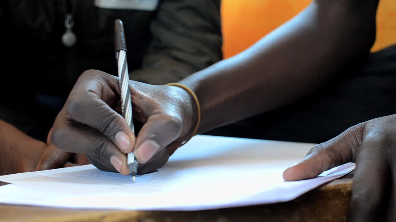 Close-up of hand of young man writing in a seminar in Kibera, Nairobi, Kenya 1