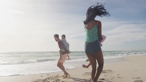 Happy-hispanic-parents-playing-with-children-on-beach-in-sun