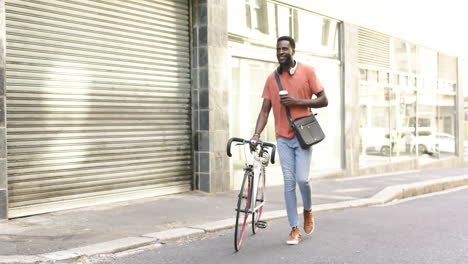 african american man walks with his bike, holding a coffee cup with copy space in the city