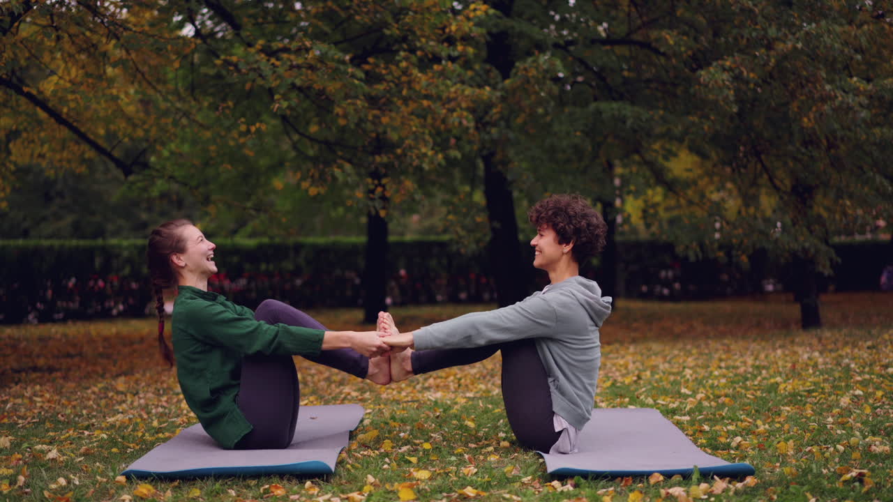 Two women practicing partner yoga in an autumn park