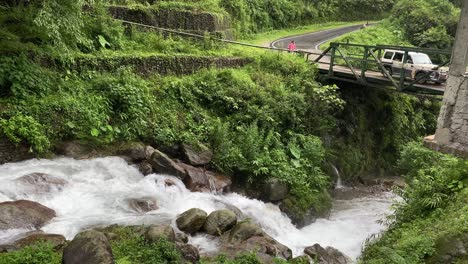 Beautiful-waterfalls-near-a-bridge-with-a-car-passing-by-a-person-in-Dooars,-India