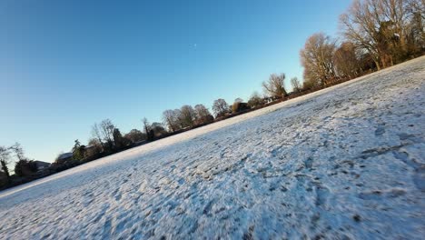 fast fpv flying across snowy sunlit winter meadow during golden hour sunrise