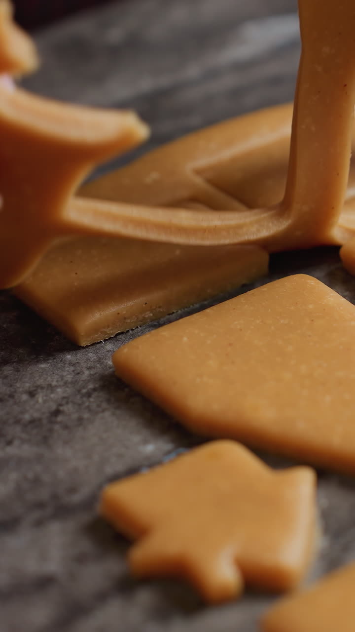 вблизи женщина осторожно удаляет избыток теста из свежерезанных форм на пекарной поверхности, готовя печенье с сложными рисунками для выпечки в уютной кухне