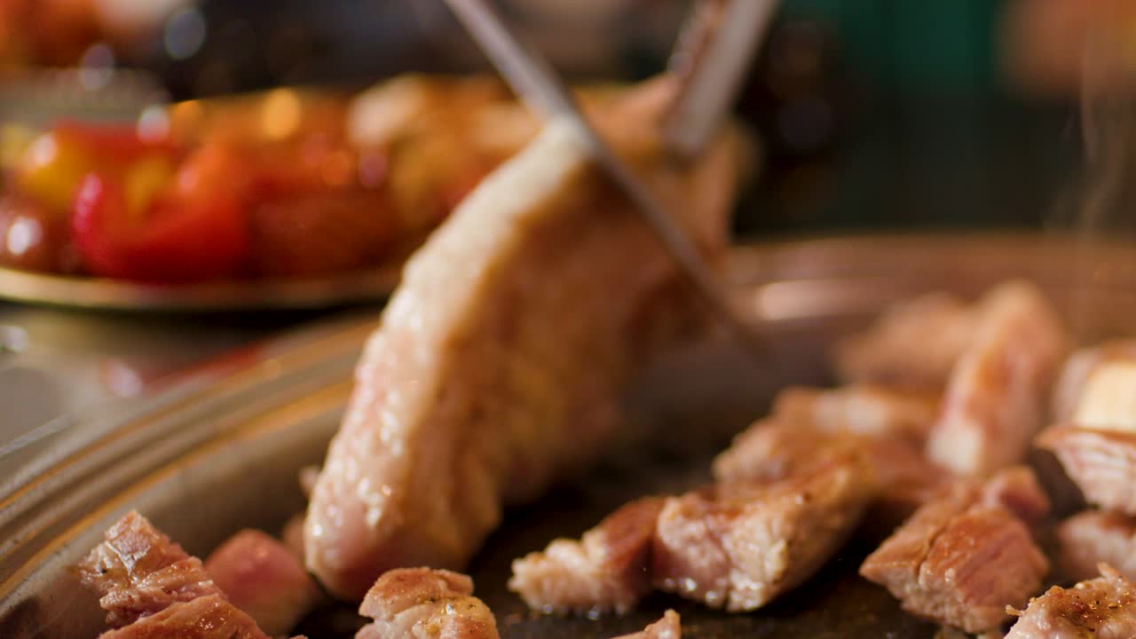 Close-up of fatty pork being sliced and grilled on hot plate, with visible smoke rising