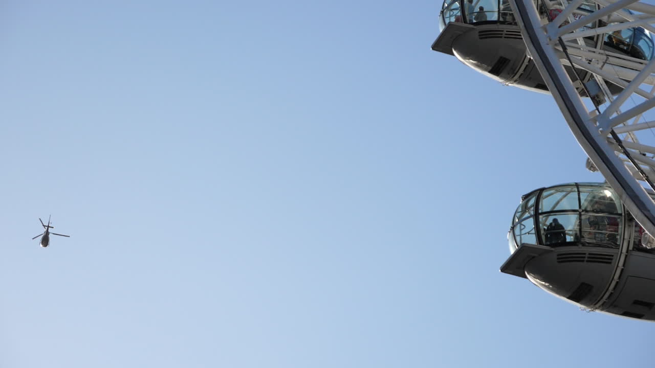 Helicopter flying over London Eye tourist attraction on sunny day, slow motion