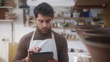 Male-Potter-In-Ceramics-Studio-Carrying-Out-Inventory-Using-Digital-Tablet