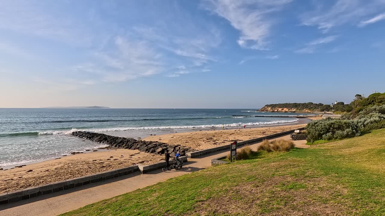 A serene beach view with gentle waves, clear skies, and a distant headland under bright daylight