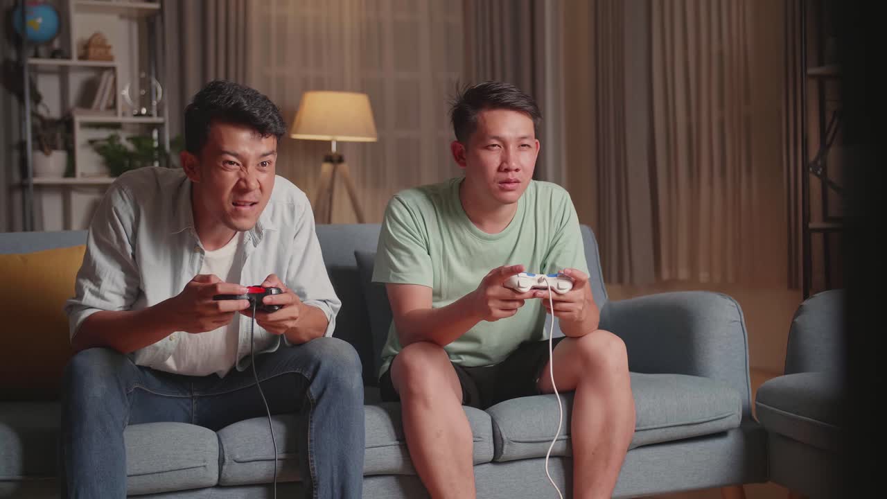 Asian Friends Playing Video Games At Home. Male Happy To Win Victory And Another Man Feeling Disappointed