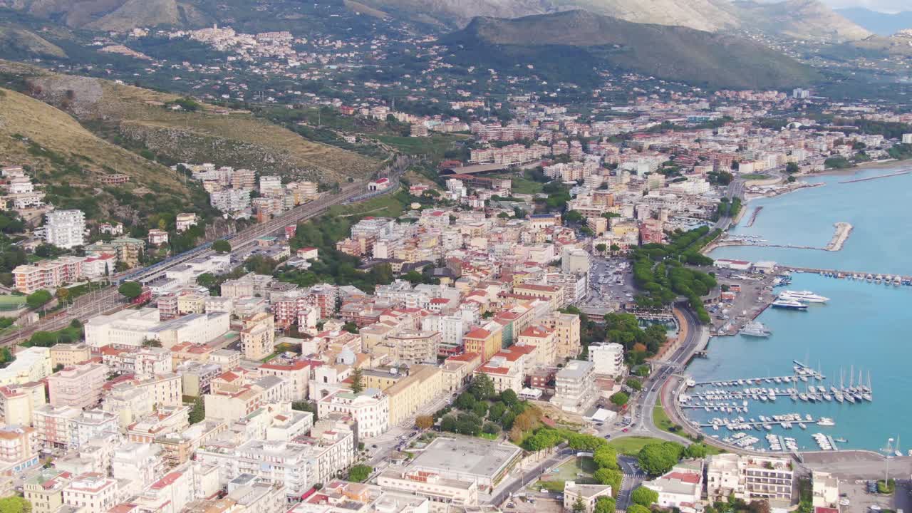 Flight above downtown city of Gaeta, buildings and boats docked at seaport marina, Italy, aerial pan right