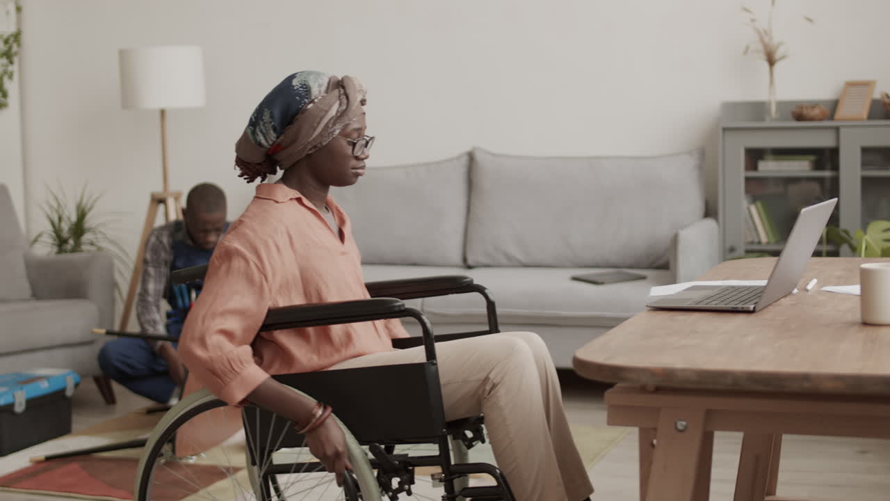 Donna con disabilità che lavora al computer mentre un falegname monta un tavolo