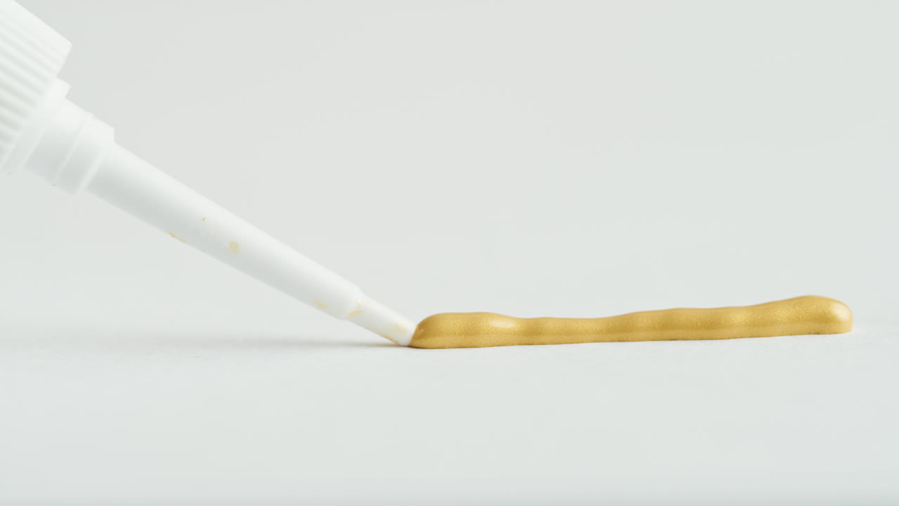 Gold Paint Dispensing from Tube onto White Surface