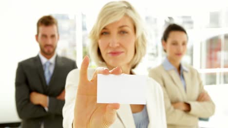 smiling businesswoman showing her card with team behind her