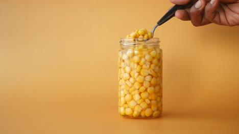 close-up of a jar of canned corn with a spoon scooping out some kernels