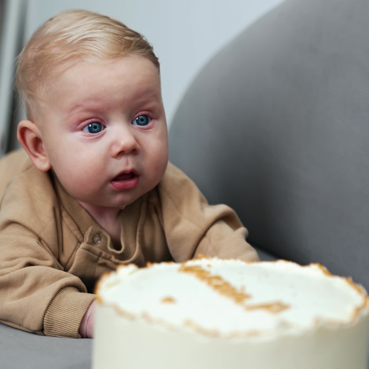 Un bebé rubio de ojos azules precioso está tumbado en un sofá. Hay una tarta grande delante de un bebé adorable.