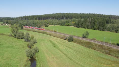 Toma-Aérea-De-Un-Tren-Db-Rojo-Moviéndose-A-Través-De-Un-Paisaje-Verde-Y-Exuberante