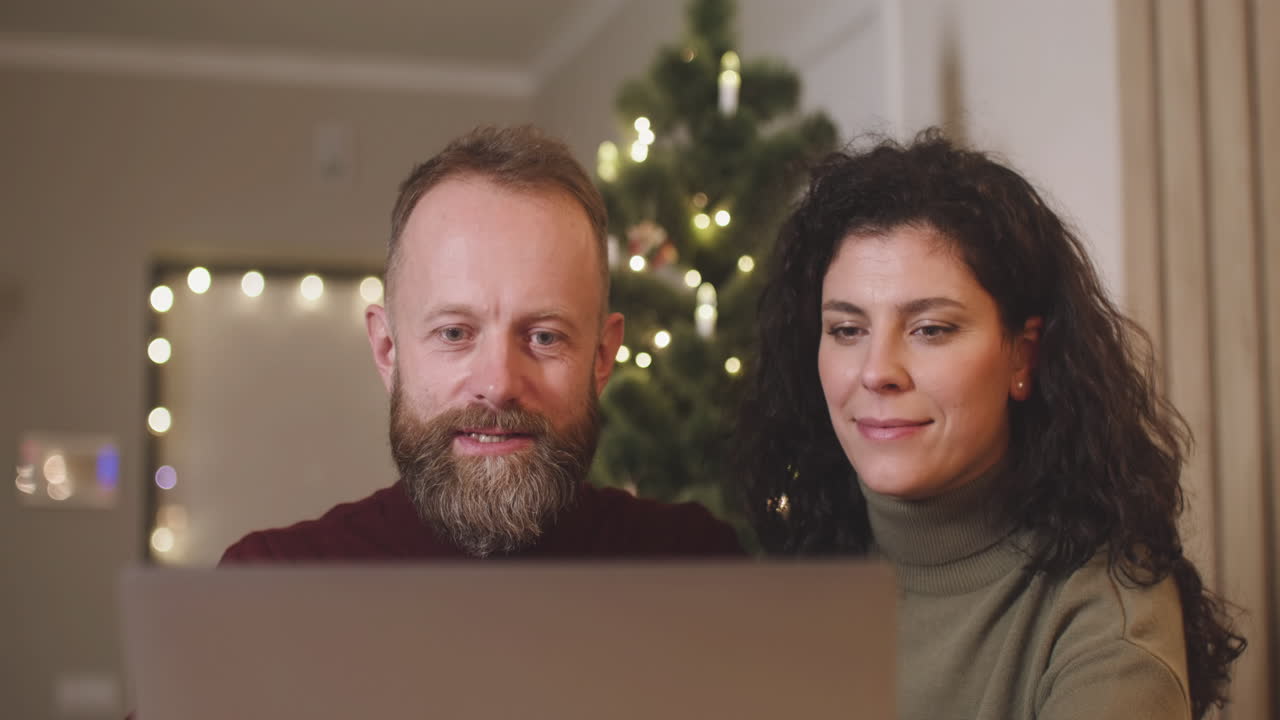 vista frontal de una pareja usando una computadora portátil en una habitación decorada con un árbol de navidad
