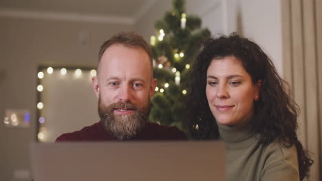 Front-View-Of-A-Couple-Using-A-Laptop-In-A-Room-Decorated-With-A-Christmas-Tree