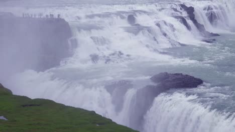 the spectacular and massive waterfall gullfoss flows in iceland with tourists on cliff in distance