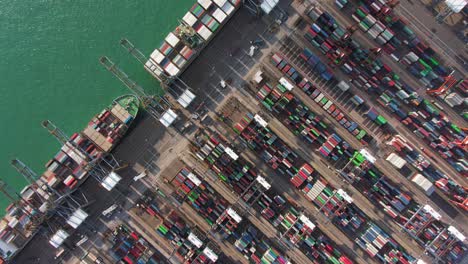 Large-Container-Ship-docked-at-Hong-Kong-commercial-port,-top-down-aerial-view-including-Stacks-of-Shipping-containers-on-a-holding-platform