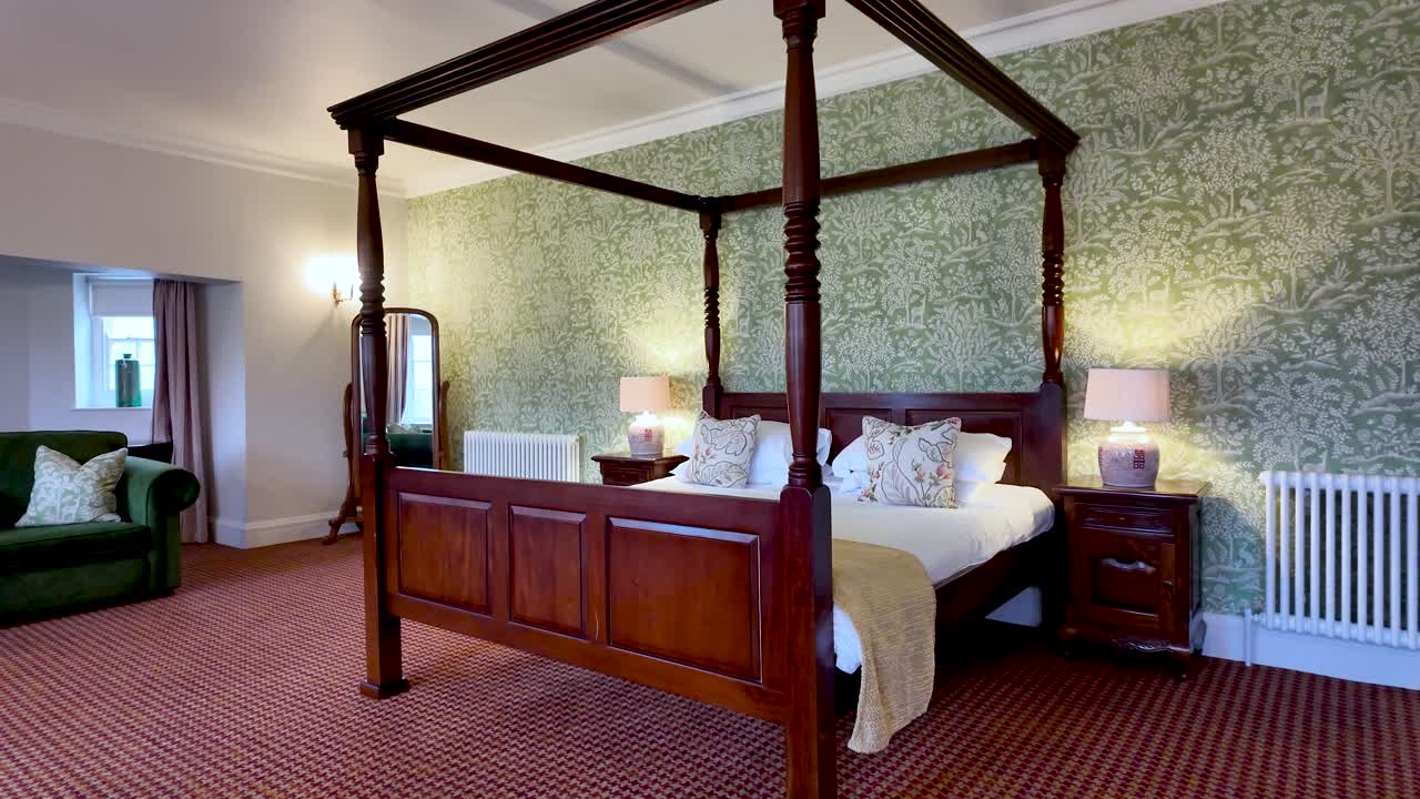 Opulenta escena de dormitorio con una cama con dosel tallada, mesitas auxiliares, lámparas y papel pintado estampado