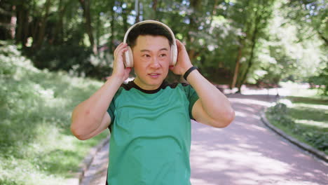 happy young japanese runner jogger man put on wireless modern headphones earphones listening music