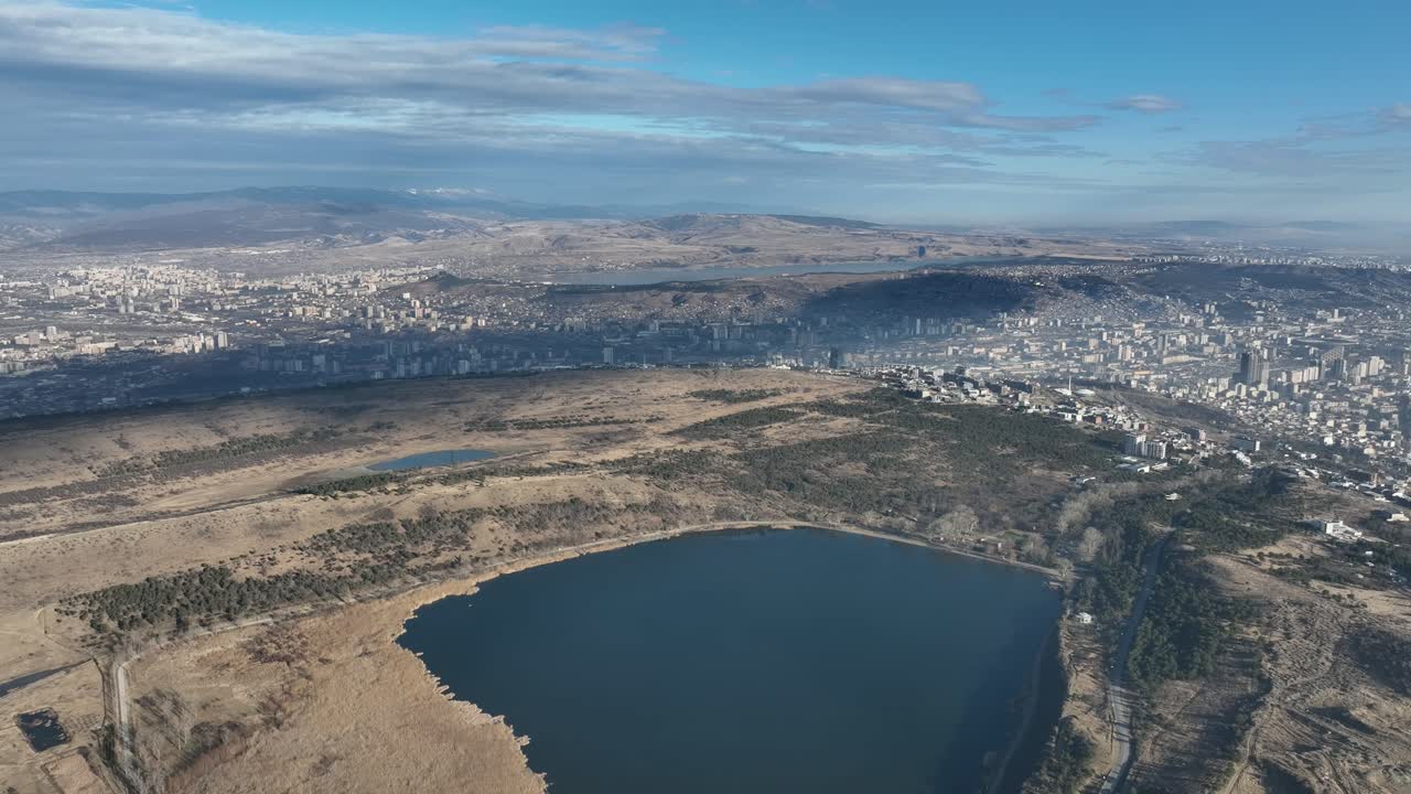 aerial view of a large city bordering a lake, with hills rolling in the background. The combination of urban development and natural scenery showcases the balance between city and nature