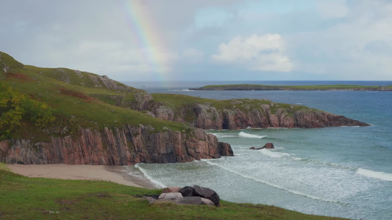 Rainbow over Ceannabeinne Beach, Durness. Green cliffs, white sand, crystal water, and island backdrop. Stunning Scottish coastal landscape with firepit foreground