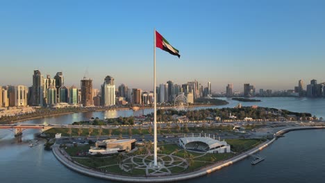 Vista-De-Drones-De-La-Bandera-De-Los-Emiratos-árabes-Unidos-Ondeando-En-El-Aire,-El-Cielo-Azul-De-Fondo,-El-Símbolo-Nacional-De-Los-Emiratos-árabes-Unidos-Sobre-La-Isla-De-La-Bandera-De-Sharjah,-Emiratos-árabes-Unidos,-Día-Nacional-De-Los-Emiratos-árabes-Unidos,-4k