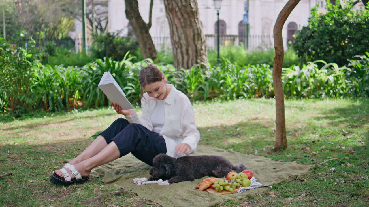 Carefree lady reading romantic novel on summer picnic with furry lovely dog