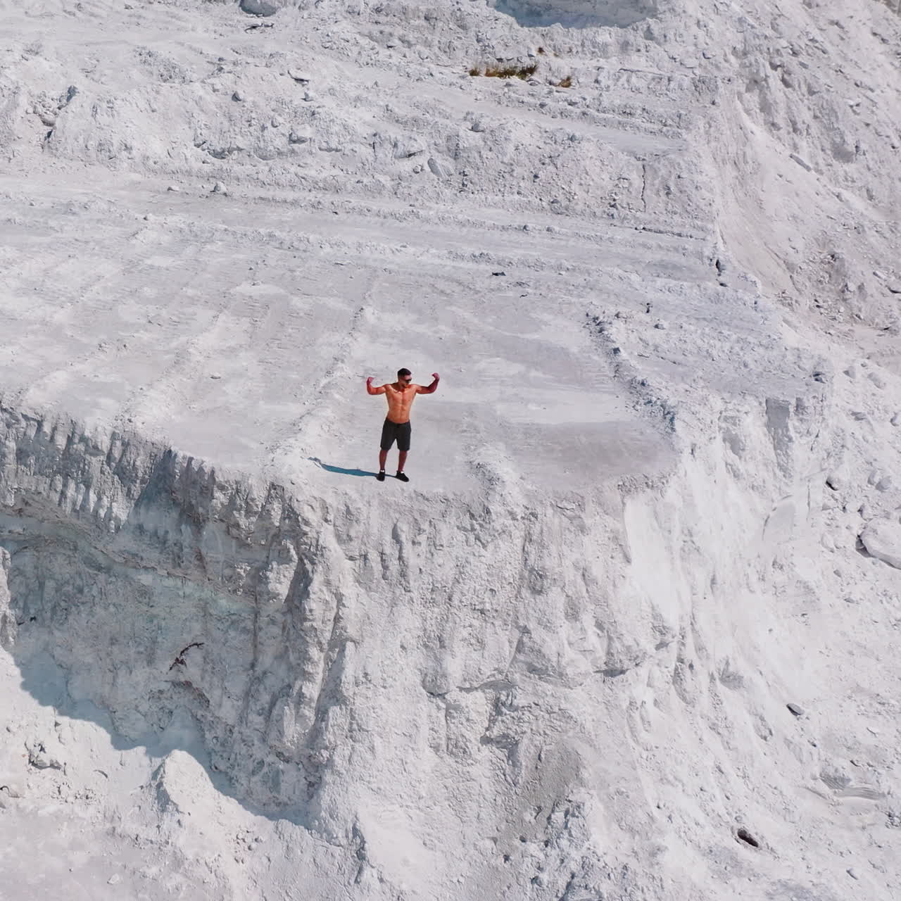 Shirtless sportsman on the rocky canyon. Aerial view of a strong man posing on the top of the hill in summer. Natural mountainous background.