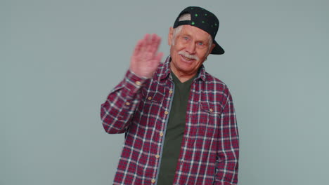 senior man smiling friendly at camera and waving hands gesturing hello or goodbye, welcoming