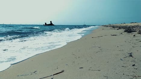 Ruhige-Aufnahme-Von-Einem-Strand-Eines-Schiffswracks,-Das-Sich-über-Einen-Goldenen-Sandstrand-Und-Das-Blaue-Meer-Des-Mittelmeers-In-Der-Nähe-Von-Thessaloniki,-Griechenland-In-Epanomi-In-Den-Ozean-Erstreckt