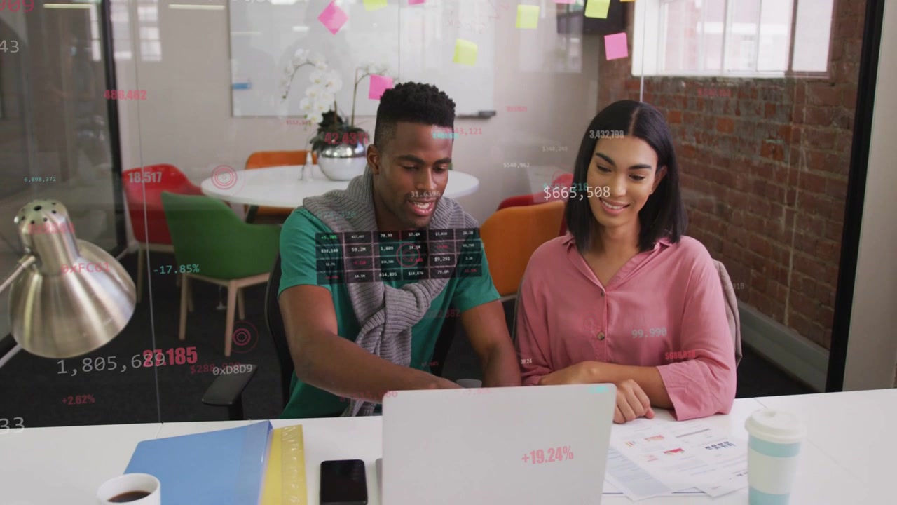 Man leaning pointing at laptop screen showing data overlays while woman reviewing data for business