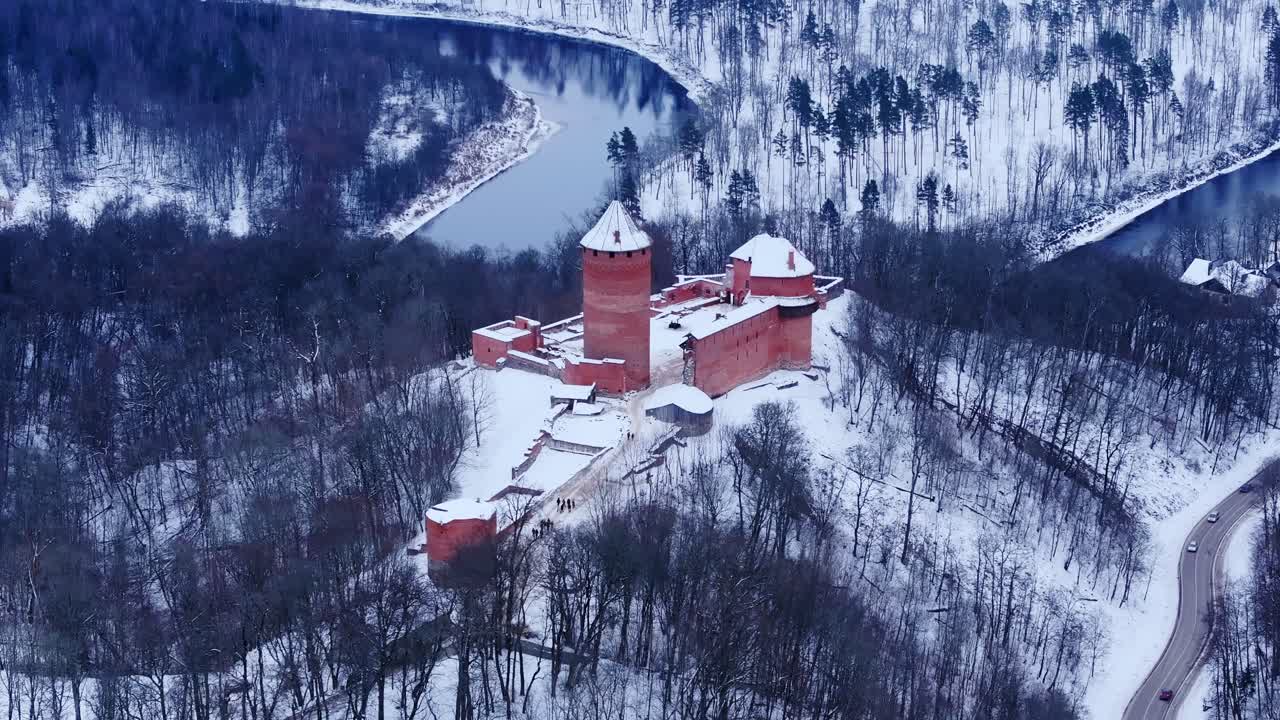 Drone glides down and tilts to show icy Turaida Castle in snowy forest Latvia