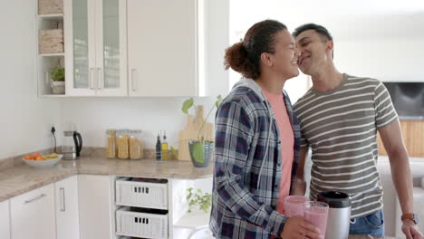 feliz pareja gay diversa haciendo batido de frutas y besándose en la cocina, espacio de copia, cámara lenta