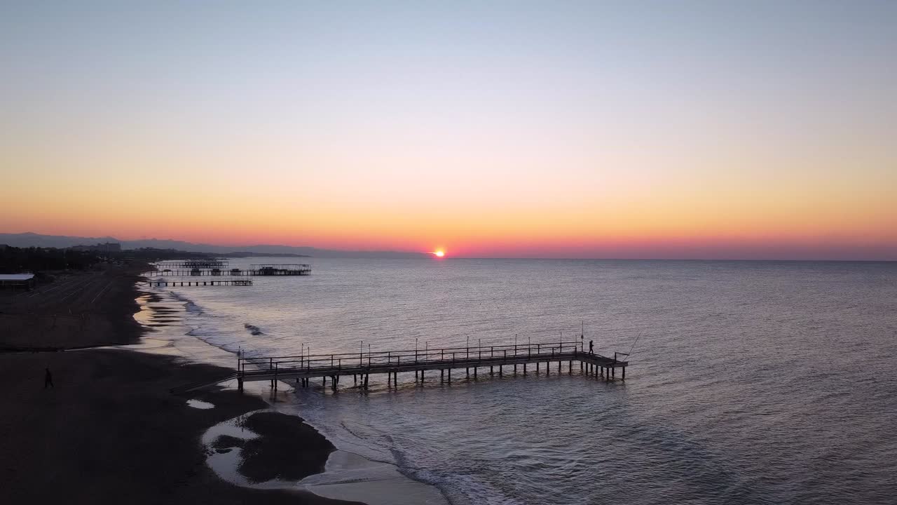 Man is walking on pier in the dawn, sun in slowly rising up, wavy sea