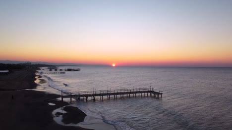 man is walking on pier in the dawn, sun in slowly rising up, wavy sea